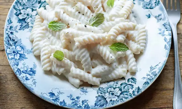 Fusilli pasta with a creamy white sauce, garnished with mint leaves, on a blue and white floral plate.