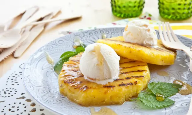 Grilled pineapple slices topped with scoops of vanilla ice cream and drizzled with honey.