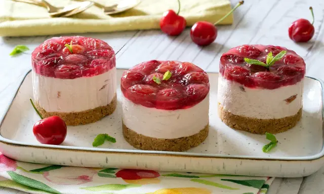 Three mini cheesecakes with cherry topping on a platter, garnished with mint leaves and fresh cherries.