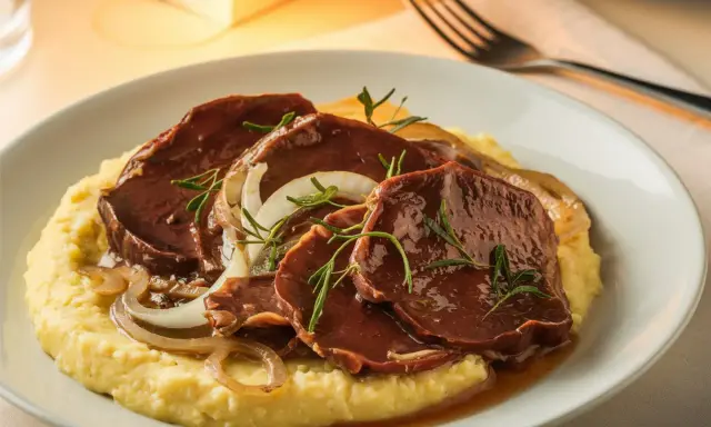 Sliced beef in sauce with onions and rosemary on a bed of polenta.