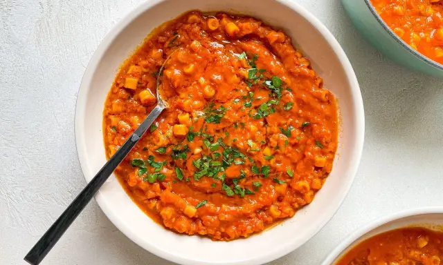 A bowl of creamy red lentil soup with small pasta and parsley, with a spoon.