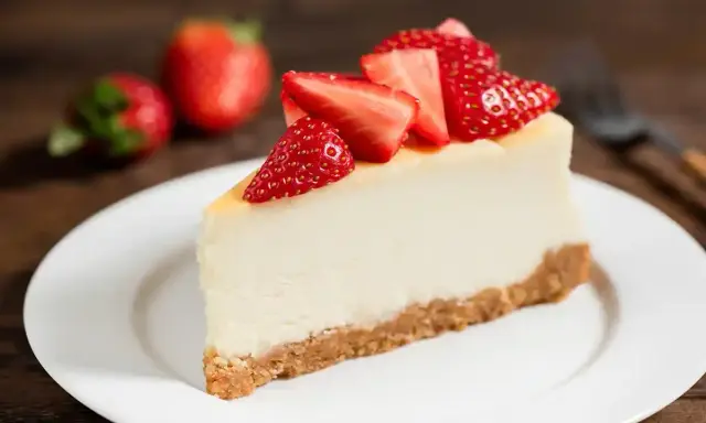Slice of cheesecake topped with fresh strawberries on a white plate.