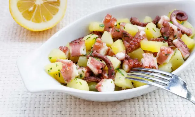 Octopus and potato salad with lemon and parsley in a white bowl.