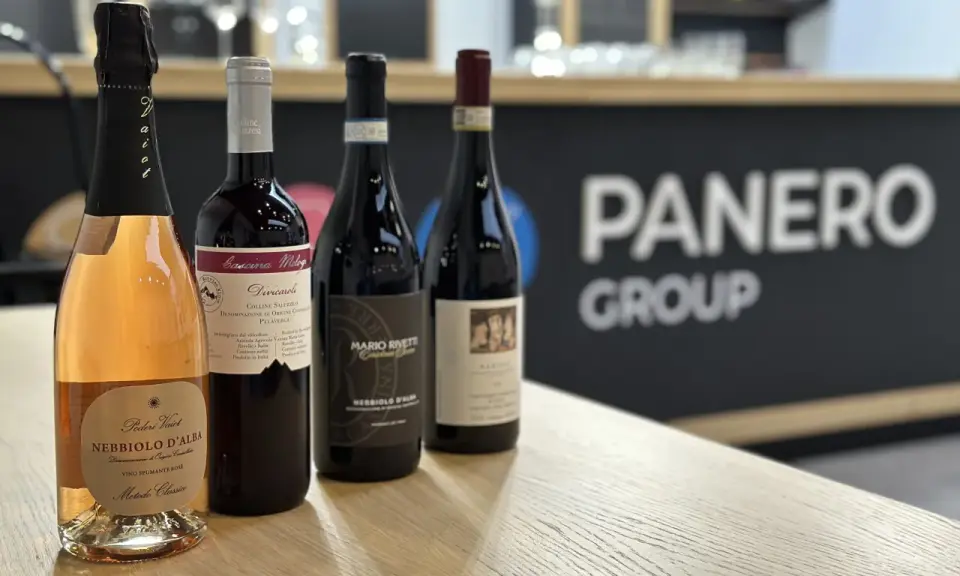 Four bottles of wine, including a rosé sparkling wine, on a wooden table with a blurred background.