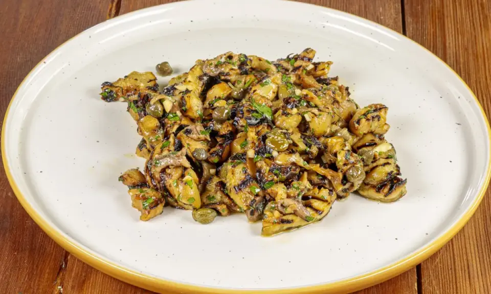 Grilled eggplant salad with capers and herbs on a white plate.