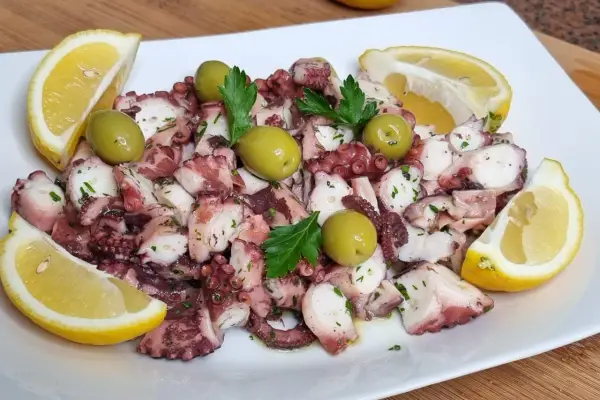Octopus salad with olives, parsley, and lemon wedges on a white plate.